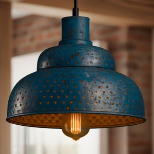 May include: A teal-coloured, industrial-style pendant light fitting with a distressed finish. The metal shade has a perforated design and houses a warm, Edison-style bulb. The fitting hangs from a black cord.