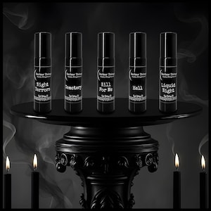 May include: Five black perfume oil bottles with the text "Night Terrors", "Cemetery", "Kill For Me", "Hell", and "Liquid Night". The bottles are displayed on a black pedestal with lit candles in front.