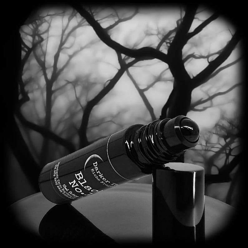 May include: A black cylindrical perfume roller bottle with a matching cap. The label features the text Darker Than, Black No. 1, and 10ml Perfume Oil. The bottle is positioned horizontally with the roller ball exposed at the top end of the container.