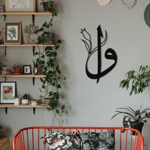 May include: Black metal wall art featuring stylized Arabic calligraphy with a floral accent. The artwork is mounted on a light gray wall, creating a striking contrast. The design adds a touch of elegance and cultural flair to any interior space.