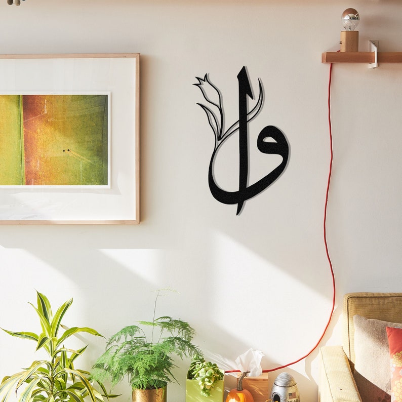 May include: Black metal wall art featuring Arabic calligraphy with a floral accent. The artwork is mounted on a white wall, creating a striking contrast. The design incorporates a stylized letterform, adding a touch of elegance to any space. This piece is ideal for home decor.