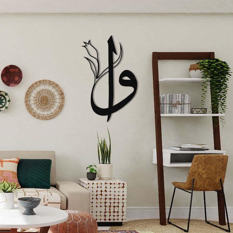 May include: A black metal wall art piece featuring Arabic calligraphy with a floral accent. The artwork is mounted on a neutral-colored wall, complementing the modern interior design. Decorative wall hangings and a wooden shelf are also visible.