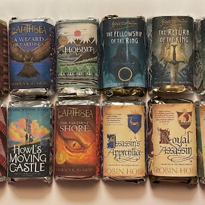 May include: A selection of wrapped books with vibrant covers. Titles include "The Tombs of Atuan," "A Wizard of Earthsea," "The Hobbit," "The Fellowship of the Ring," and "The Two Towers." Other titles are "Howl's Moving Castle" and "Assassin's Apprentice."