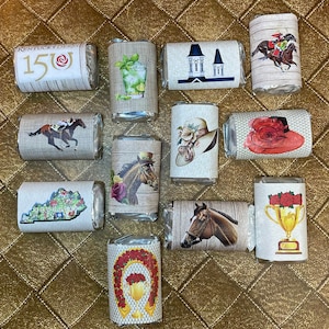 May include: A collection of 10 small, wrapped chocolate bars with various designs related to the Kentucky Derby. The designs include a horse racing scene, a mint julep, a horseshoe, a trophy, a hat, and a map of Kentucky.