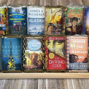 May include: A collection of 12 paperback books with various titles and authors. The books are arranged in two rows of six, with the spines facing the viewer. The books are all different colors and have different designs on their covers.