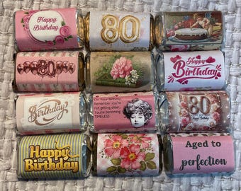 May include: Twelve pink and white chocolate bar wrappers with various birthday designs. The wrappers feature the numbers 80 and 20, the words "Happy Birthday", "Birthday", and "Aged to perfection", and floral and vintage-inspired designs.