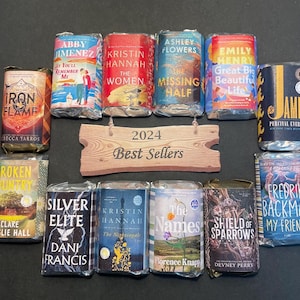 Op de afbeelding: Een verzameling verpakte boeken, met titels als "Iron Flame", "The Women" en "The Missing Half". Een houten bord leest "2024 Best Sellers". De boeken zijn in verschillende kleuren, met tekst zichtbaar op de covers.