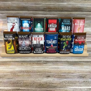 May include: A display of Freida McFadden books on a wooden shelf. The book covers are in various colours and feature titles such as "The Coworker," "The Inmate," and "The Locked Door." The author's name is visible on each book.
