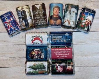 Könnte beinhalten: Eine Sammlung von verpackten Schokoriegeln mit weihnachtlichen Designs. Die Verpackungen zeigen Bilder und Zitate aus dem Film "Schöne Bescherung". Die Schokoriegel sind auf einer hellen Holzoberfläche angeordnet.