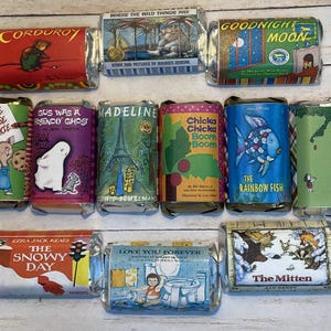 Op de afbeelding: Een verzameling verpakte snoeprepen met boekomslagen. Titels zijn onder meer "Corduroy", "Where the Wild Things Are", "Goodnight Moon", "If You Give a Mouse a Cookie", "Gus Was a Friendly Ghost", "Madeline", "Chicka Chicka Boom Boom", "The Rainbow Fish", "The Snowy Day", "Love You Forever" en "The Mitten".