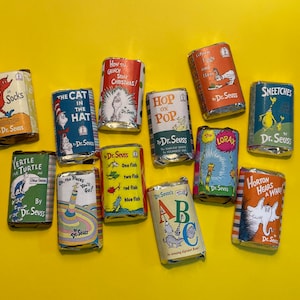 Peut inclure: Une collection de 12 barres de chocolat sur le thème des livres de Dr. Seuss. Les barres sont enveloppées dans du papier d'aluminium et présentent des illustrations de livres populaires de Dr. Seuss, notamment "Le Chat dans le Chapeau", "Oeufs Verts et Jambon", "Horton entend un Qui!" et "Saute sur Pop".