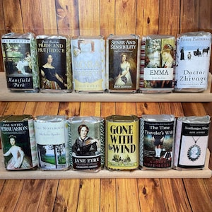 May include: A shelf with ten different book-themed soap bars. The soaps are wrapped in paper with book covers and titles. The titles include "Pride and Prejudice", "Sense and Sensibility", "Emma", "Doctor Zhivago", "Persuasion", "The Notebook", "Jane Eyre", "Gone With the Wind", "The Time Traveler's Wife", and "Northanger Abbey".