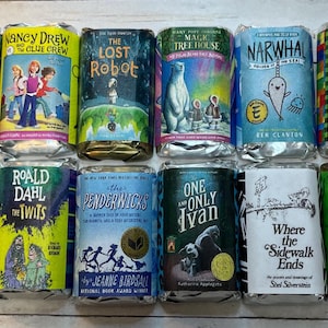 May include: A collection of children's books, each wrapped in silver foil. Titles include "Land of Stories," "Nancy Drew," "The Lost Robot," "Magic Tree House," "Narwhal," and "Diary of a Wimpy Kid." Other titles are "Ramona the Pest," "The Twits," "The Penderwicks," "One and Only Ivan," and "Where the Sidewalk Ends."