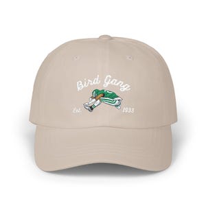 May include: A beige baseball cap with a curved brim. The cap features the text "Bird Gang" in white script above an embroidered image of a football player in green and white. The year "1933" is below the image.