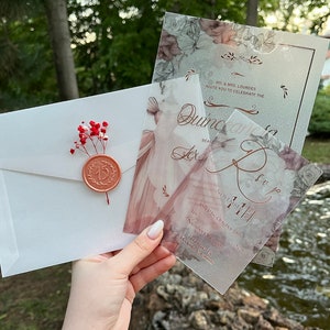 May include: A set of three translucent invitations with a floral design and gold lettering. The invitations are for a Quincea&ntilde;era celebration. The text on the invitations reads "Quincea&ntilde;era Lex" and "November 11, 2021".