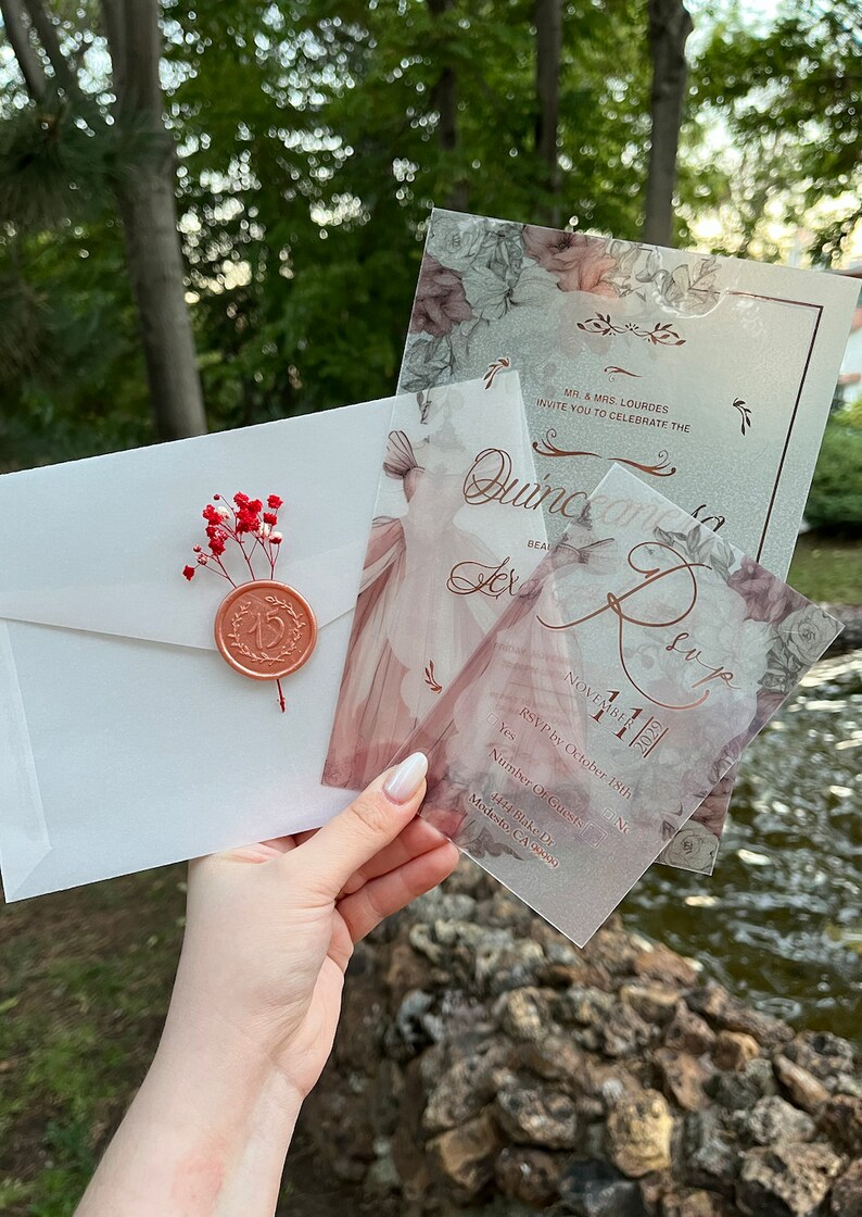 May include: A set of three translucent invitations with a floral design and gold lettering. The invitations are for a Quincea&ntilde;era celebration. The text on the invitations reads "Quincea&ntilde;era Lex" and "November 11, 2021".