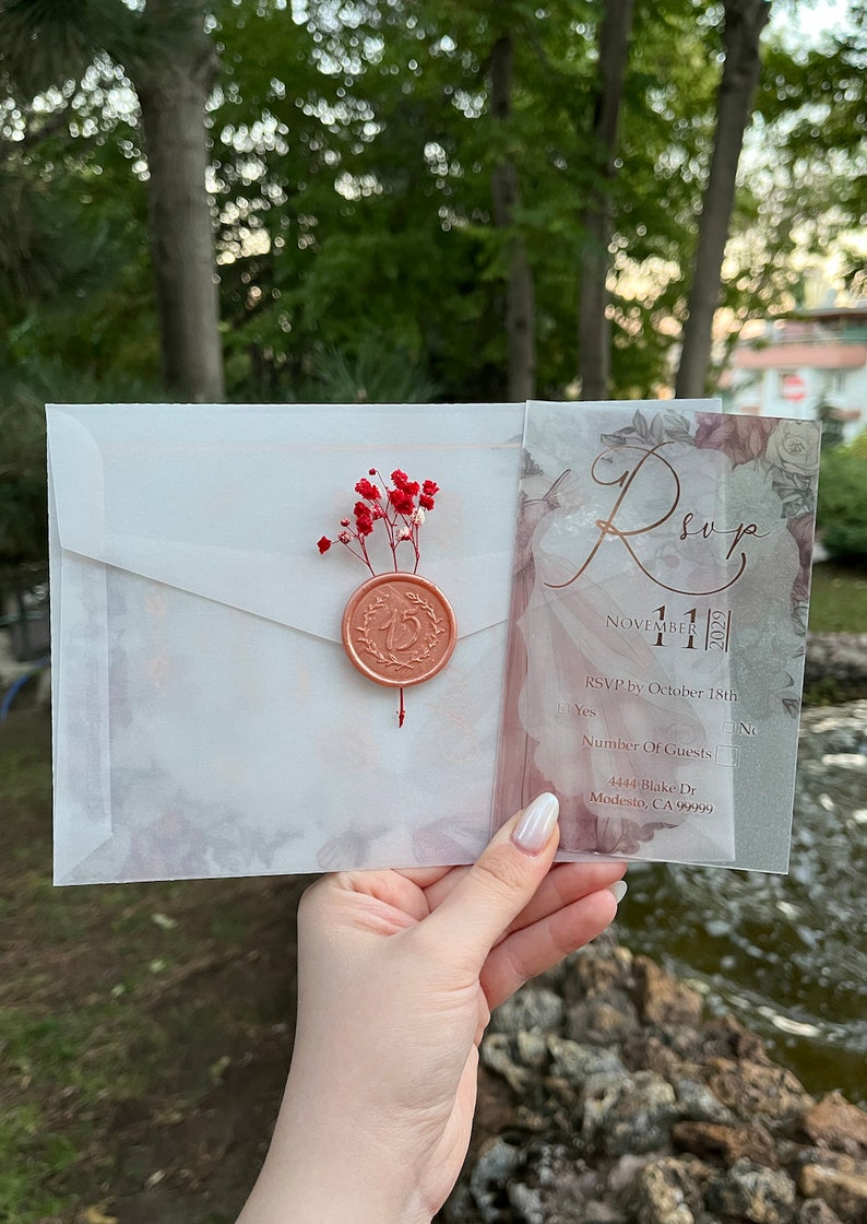 May include: A clear, translucent RSVP card with a floral design and gold lettering. The card includes the date "November 11, 2023" and an RSVP deadline of October 18th. The address is 4444 Blake Dr, Modesto, CA 99999.