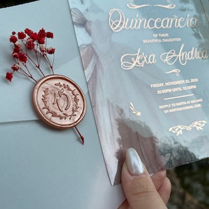 May include: A light blue invitation with gold lettering for a Quincea&ntilde;era celebration. The invitation features the name "Lexa Andrea" and the date "Friday, November 22, 2029".