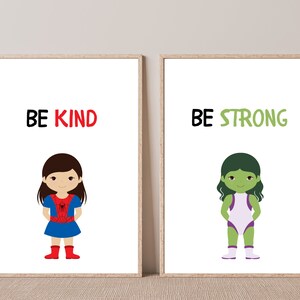 May include: Two framed art prints with cartoon illustrations. One print says "BE KIND" above a girl in a blue dress and red boots. The other says "BE STRONG" above a green-skinned character in a white and purple outfit.