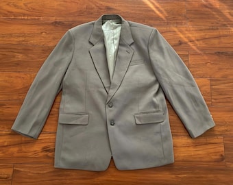 May include: A grey blazer with a two-button fastening, notched lapels, and two front pockets. The jacket has long sleeves and a light green lining. The blazer is laid flat on a wooden surface.