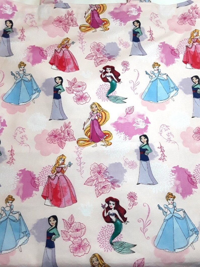 Może przedstawiać: R&oacute;żowy materiał z powtarzającym się wzorem księżniczek Disneya. Księżniczki to Kopciuszek, Ariel, Bella, Mulan, Rapunzel i Aurora. Materiał zawiera r&oacute;wnież r&oacute;żowe kwiaty i liście.