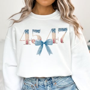 May include: White sweatshirt with the numbers 4547 printed in red, white, and blue, resembling the American flag. A blue bow is centered below the numbers.