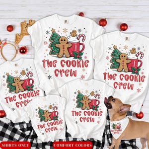 May include: White t-shirts with a Christmas-themed design. Each shirt features a gingerbread man, a Christmas tree, and a mug of hot cocoa, with the text "The Cookie Crew". A dog wears a matching bandana.