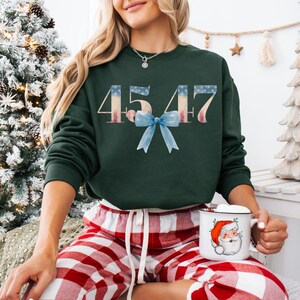 May include: A green sweatshirt with the numbers 45 47 printed in white with a red, white, and blue American flag design. A blue bow is centered between the numbers.