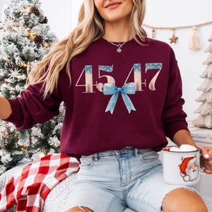 May include: A maroon sweatshirt with the number 4547 printed in white with a red, white, and blue design. A blue bow is centered below the number.