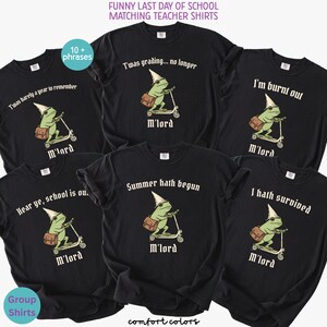 May include: Black Comfort Colors t-shirts with various phrases for teachers, including "Twas grading... no longer" and "Summer hath begun." Each shirt features a cartoon frog riding a scooter, wearing a dunce cap and carrying a satchel. Text at the bottom reads "M'lord."