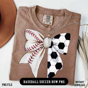 Peut inclure: T-shirt marron avec un motif de nœud papillon combinant un ballon de baseball et un ballon de football. Le côté baseball est blanc avec des coutures rouges, le côté football est noir et blanc. Un collier argenté est visible.