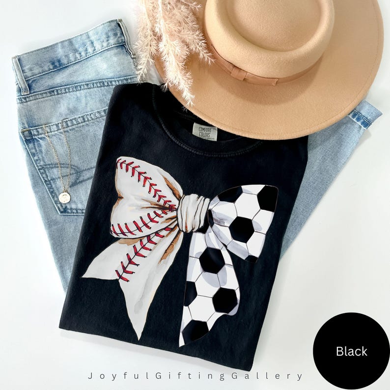 May include: Black t-shirt with a white bow design featuring a baseball and soccer ball pattern. The text "Joyful Gifting Gallery" is visible at the bottom of the image.