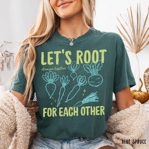 May include: A teal t-shirt with the slogan "LET'S ROOT" in lime green, with the words "stronger together" and "FOR EACH OTHER." The design includes light blue illustrations of root vegetables such as carrots and beets.