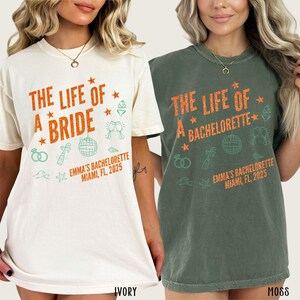 May include: Ivory and moss green t-shirts with orange text and green illustrations. The ivory shirt reads "THE LIFE OF A BRIDE" with "EMMA'S BACHELORETTE MIAMI, FL, 2025" below. The moss green shirt reads "THE LIFE OF A BACHELORETTE" with the same text.