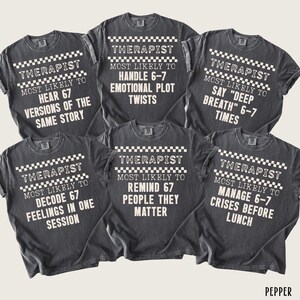 May include: Six dark gray t-shirts with white text and a checkered pattern. Each shirt reads "THERAPIST" and "MOST LIKELY TO" followed by a humorous statement about therapists, such as "HEAR 67 VERSIONS OF THE SAME STORY."