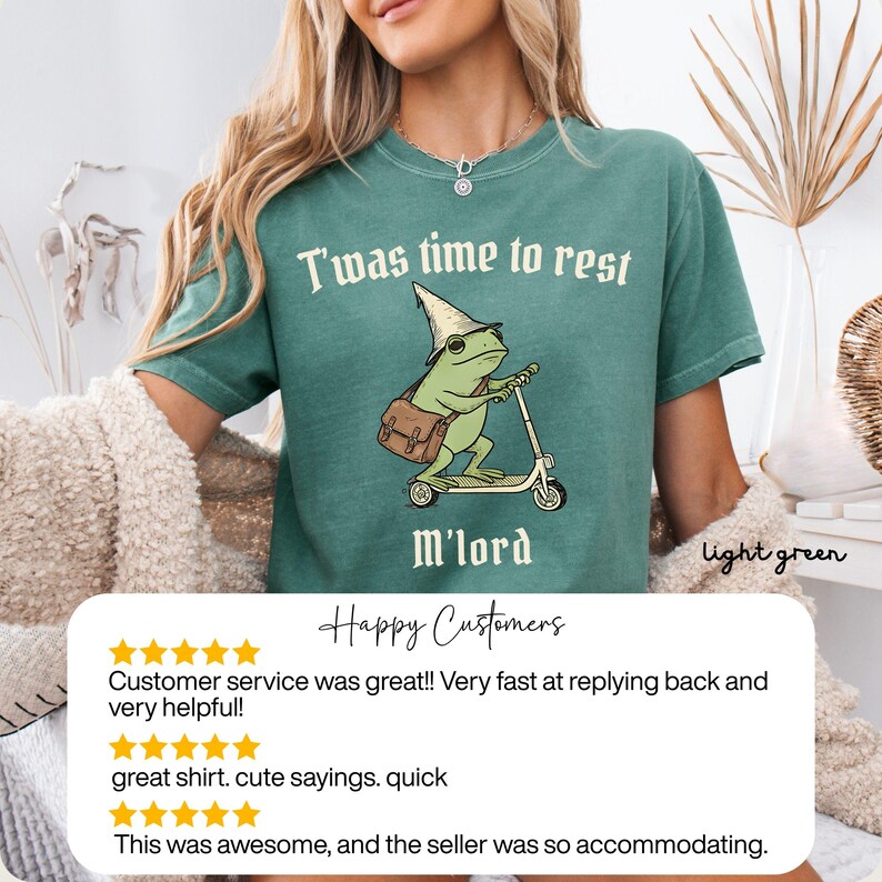 May include: Light green t-shirt with the text "T'was time to rest M'lord". The shirt features a cartoon frog riding a scooter and wearing a wizard hat. The shirt is light green.
