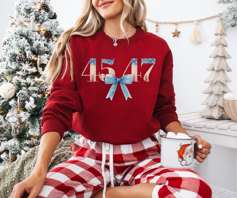 May include: Red sweatshirt with the number 4547 printed in white with a blue bow. The sweatshirt is worn by a person wearing red and white plaid pajama pants.