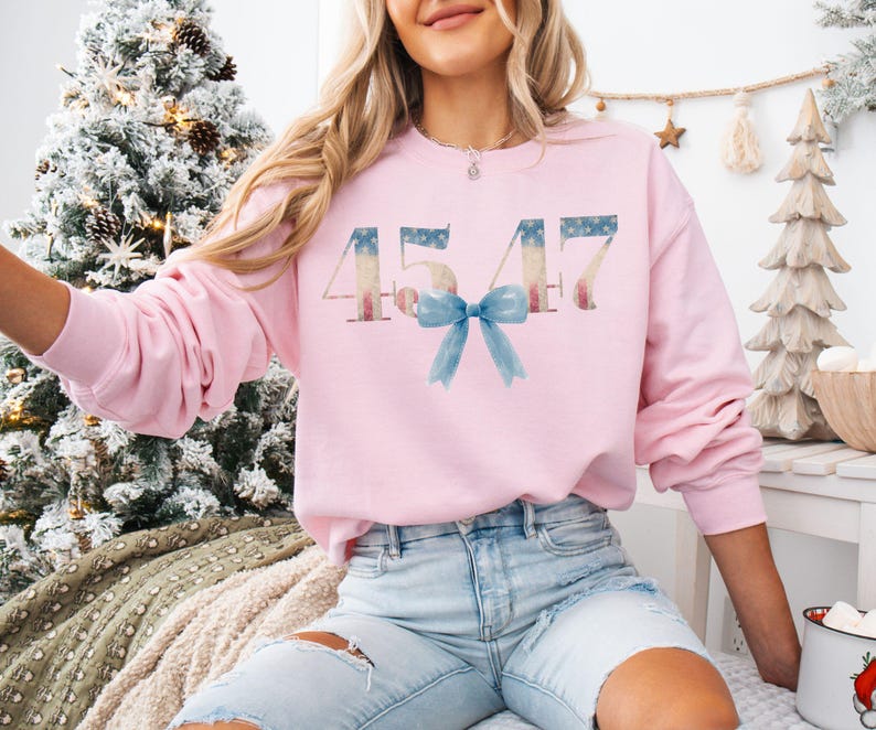 May include: A pink sweatshirt with the number 4547 printed on it in a distressed American flag design. A blue bow is centered below the number.