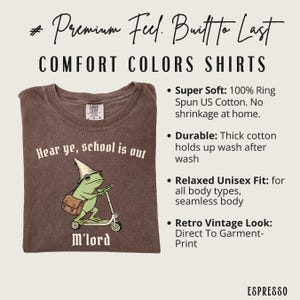 May include: Espresso-colored Comfort Colors t-shirt with a graphic of a frog on a scooter, wearing a wizard hat and carrying a satchel. Text reads "Hear ye, school is out" and "M'lord". The shirt is made of 100% ring-spun US cotton.