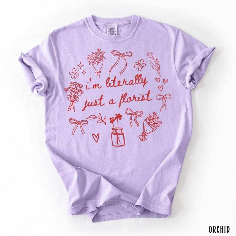 May include: A light purple t-shirt with the text "I'm literally just a florist" in red. The design includes red floral illustrations, bows, and hearts. The word "ORCHID" is printed in the bottom right corner.