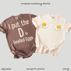 May include: Two matching t-shirts. One is espresso-coloured with the text "I put the D in Deviled Eggs." The other is ivory-coloured with two devilled egg graphics. The text "couples matching shirts" is at the top.