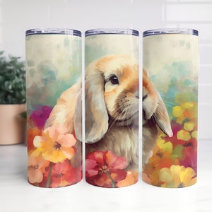 May include: A white and brown bunny with floppy ears is surrounded by colorful flowers. The bunny is painted in a watercolor style on a white background. This image is printed on a stainless steel tumbler.