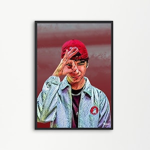 Op de afbeelding: Een ingelijste kunstdruk met een gestileerd portret van een persoon die een rode baseballcap en een lichtblauwe jas draagt. De persoon maakt een 'oké' handgebaar. De achtergrond is een verloop van rood en grijs.