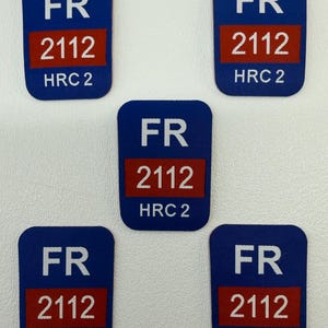 Puede incluir: Cinco parches rectangulares azules con esquinas redondeadas. Cada parche tiene las letras "FR" en blanco en la parte superior, un rectángulo rojo con el número "2112" en blanco y "HRC 2" en blanco en la parte inferior.