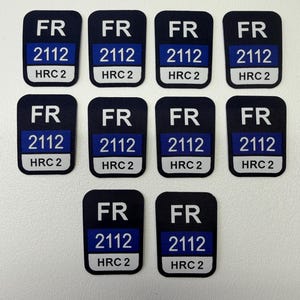 Puede incluir: Un conjunto de diez parches rectangulares. Cada parche es de color azul marino con texto blanco que dice "FR", "2112" y "HRC 2". El texto está dispuesto en tres líneas con una franja azul en el medio.