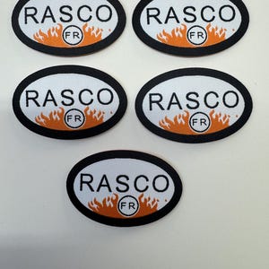 May include: Five oval-shaped patches with the word "RASCO" in white capital letters. Below the text is a flame design in orange and yellow. The patches have a black border and the letters "FR" in a circle.