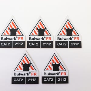 May include: Five triangular safety labels with a black silhouette inside a red and white striped triangle. The labels read "Bulwark FR", "CAT2", and "2112".
