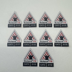 May include: A collection of ten triangular safety labels. Each label features a red and white striped hazard symbol, a black silhouette, and the text "Bulwark FR", "CAT2", and "2112".