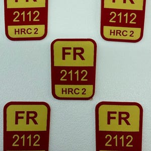 Puede incluir: Cinco parches rectangulares con esquinas redondeadas. Cada parche tiene un fondo rojo con un rectángulo amarillo en la parte superior que contiene las letras "FR". Debajo, se muestra el número "2112", seguido de "HRC 2".