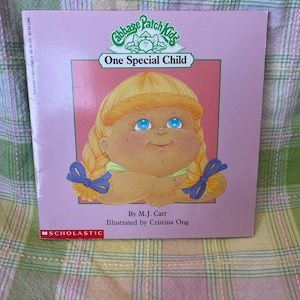 May include: A pink children's book cover for "One Special Child" with a Cabbage Patch Kids illustration. It features a blonde doll with blue eyes. The book is published by Scholastic. The cover also includes the author and illustrator.